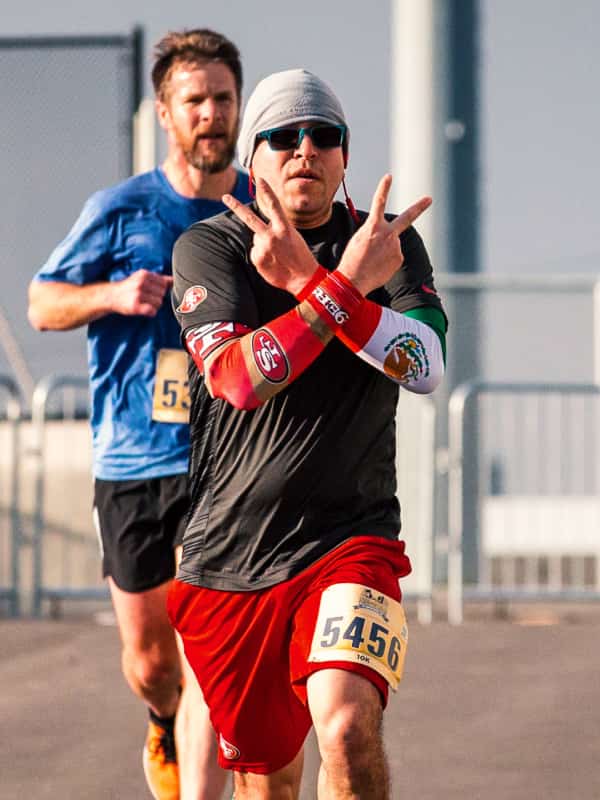 A participant in the 2019 Golden Heart Run flashes peace signs at the camera as he runs past.