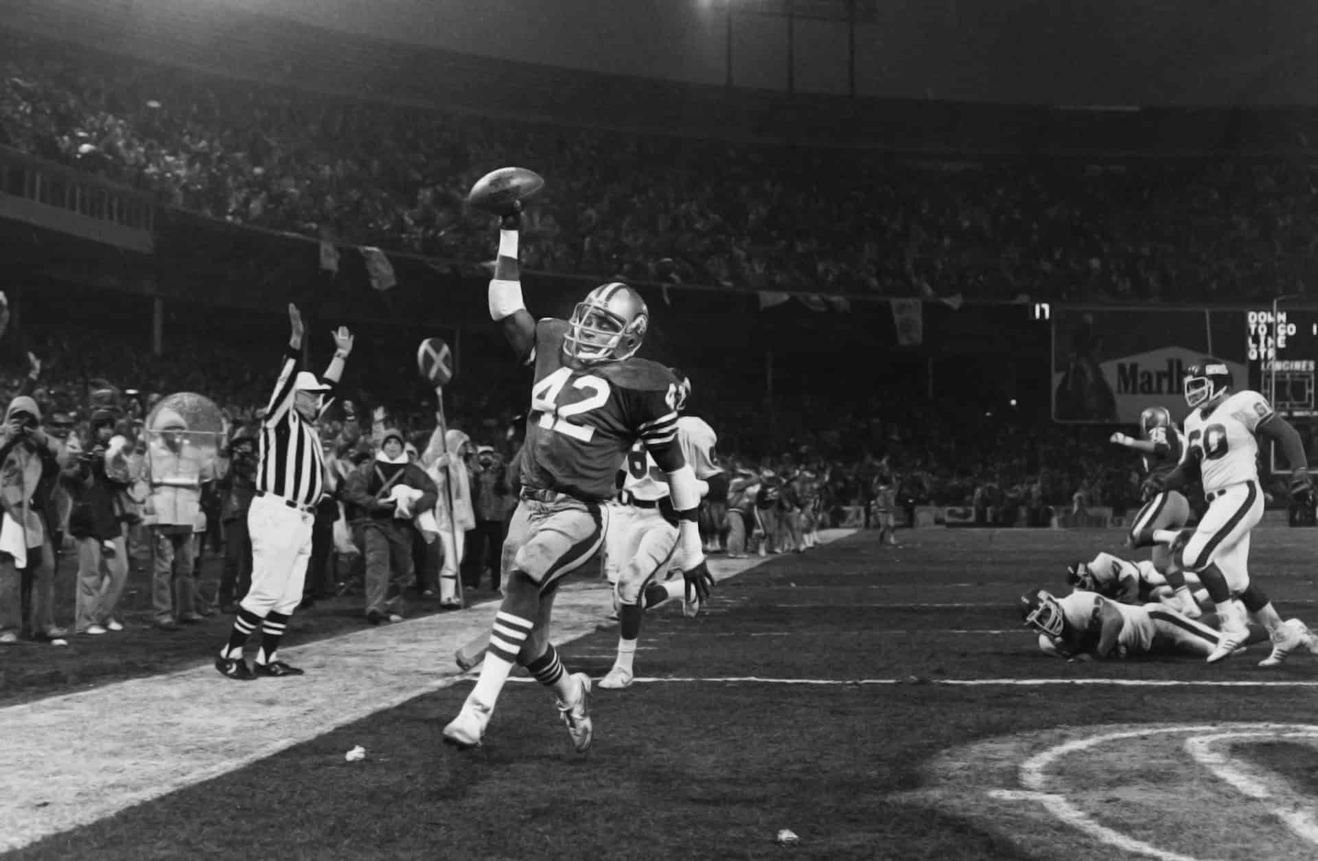 Number 42 raises the ball in celebration as a referee behind him calls a touchdown.